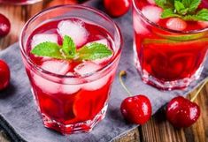 two glasses filled with ice and cherries on top of a wooden table next to some strawberries