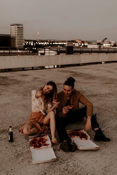 a man and woman sitting on the ground eating pizza