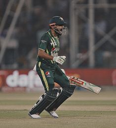 a cricket player is walking on the field with his bat in hand and helmet down