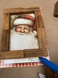 a wooden frame with a painting of a santa clause on it and a blue pen next to it