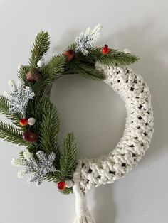 a crocheted christmas wreath with pine cones, berries and fir needles hanging on a white wall