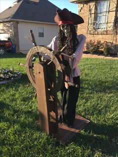 a man dressed as a pirate holding a wooden wheel and wearing a straw hat standing in front of a house