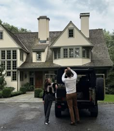 two people standing in front of a large house with a truck parked next to it