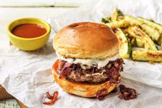 a hamburger and some fries on a piece of wax paper next to a bowl of dipping sauce