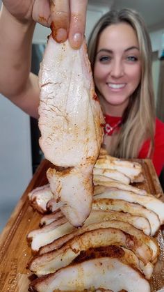 a woman holding up a piece of meat on a cutting board