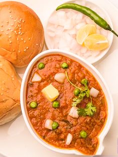 a white plate topped with two buns and a bowl filled with chili next to bread