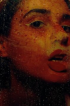 a woman looking out the window with rain drops on her face and nose, in front of a red background