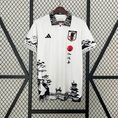 a white polo shirt with black and red designs on it, hanging against a fence