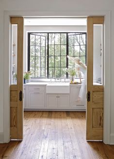 an open door leading to a kitchen with wooden floors and white cabinets, along with windows