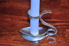 a white candle sitting on top of a wooden table next to a metal holder with a ring around it