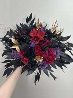 a bouquet of flowers is being held up by someone's hand in front of a white wall