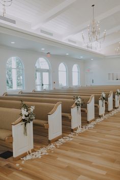 rows of pews with flowers on them in a large room filled with windows and chandeliers