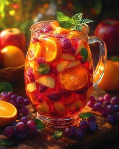 a pitcher filled with oranges, raspberries and mint leaves on top of a wooden table