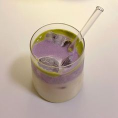 a glass filled with purple liquid next to an orange and lime slice on a white table