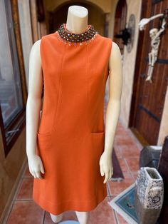 Stunning mod shift dress by Carlye in a warm orange color. Two shallow pockets at each hip, zips up the back with a Scovil Zip, two hook and eye closures at the nape of the neck.  Unlined, the fabric is a thick cotton jersey, it could be a wool blend, just by the weight, but I'm not certain as there are no labels to indicate such; but the fabric is not itchy. The jeweled trim at the neck is in perfect condition, not missing a single jewel. The dress is in excellent condition, there is an area of small snags on the front of the dress and loose threads at the eye part of the closure in back, last three photos. Measurements taken while lying flat, doubled when necessary: Bust: 36" Waist: 32" Hips: 40" Armscye: 16" Length: 38" Neck: 15" Mod Shift Dress, 70s Orange, Eye Parts, Dress Clothes For Women, Festival Season, Shift Dress, Orange Color, Wool Blend, The Dress