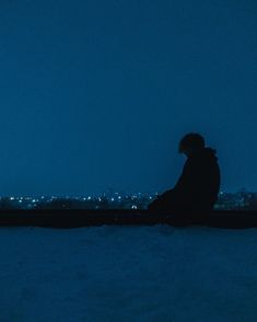 a person sitting in the snow at night with their back to the camera looking out