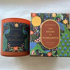 an orange candle sitting next to a box with the words, the souks of marrakeh on it