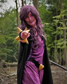 a woman dressed in purple and black holding a yellow star shaped object while standing next to trees