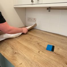 a person with a blue object on top of a wooden counter in a kitchen next to white cabinets