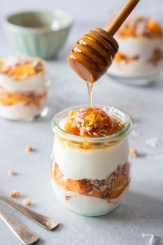 a spoon drizzling honey onto some food in small glass jars on a table