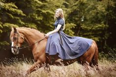 a woman riding on the back of a brown horse in a field with tall grass