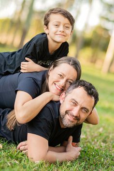 a man and woman laying in the grass with their child on her back, smiling