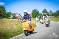 several people riding scooters on a road in the countryside, one person is wearing a helmet