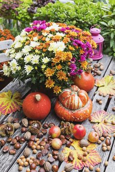 an arrangement of flowers, pumpkins and acorns sitting on a wooden table