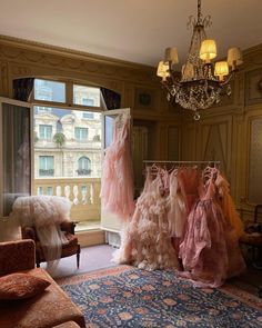 there are many dresses hanging on the rack in this room with chandelier and couches