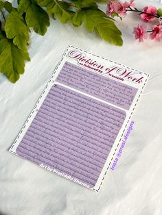 a piece of paper sitting on top of a table next to pink flowers and green leaves