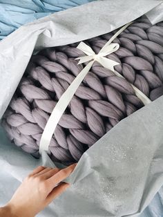 a hand holding a large gray blanket wrapped in white paper and tied with a ribbon