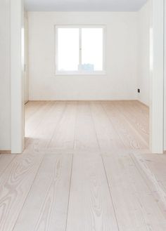 an empty room with white walls and wood flooring in the foreground is a window