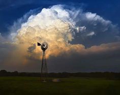 a large cloud looms over a windmill in the middle of a field