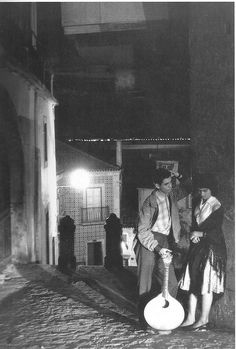 a man and woman standing on the side of a street next to a building at night