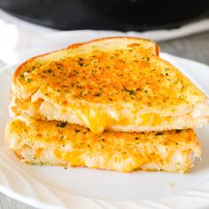 two grilled cheese sandwiches on a white plate with a skillet in the background