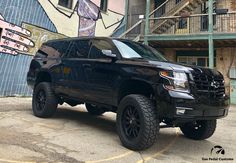 a black truck parked in front of a building with graffiti on the wall behind it