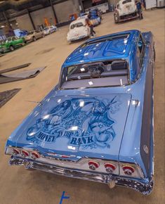 an old blue car is parked in a garage with other cars and trucks behind it