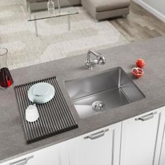 a kitchen sink sitting on top of a counter next to a wine glass and fruit