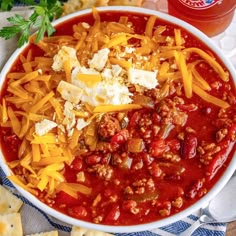 a bowl filled with chili and cheese next to crackers