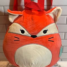 an orange and white bag with a fox face on it's side hanging from a hook