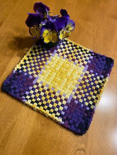 a purple and yellow placemat with flowers on it sitting on a wooden table next to a vase