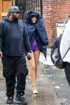 a man and woman walking down the street in front of a brick building, one wearing a hoodie