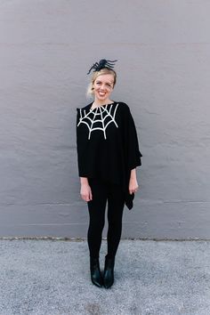 a woman standing in front of a gray wall wearing a spider web sweater and black leggings