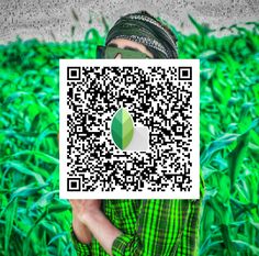 a man holding up a qr code in front of a field of green grass