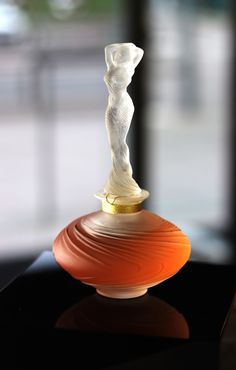 an orange vase sitting on top of a black table in front of a window with a white statue