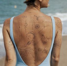 the back of a woman's body with drawings on it and an ocean in the background