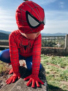 a young boy dressed as spider man sitting on top of a rock