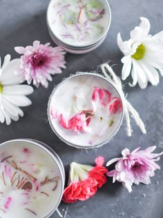 three glasses filled with white and pink flowers on top of a gray surface next to daisies