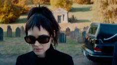 a woman wearing sunglasses standing in front of a cemetery