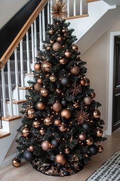 a decorated christmas tree with gold and black ornaments on it in front of a staircase